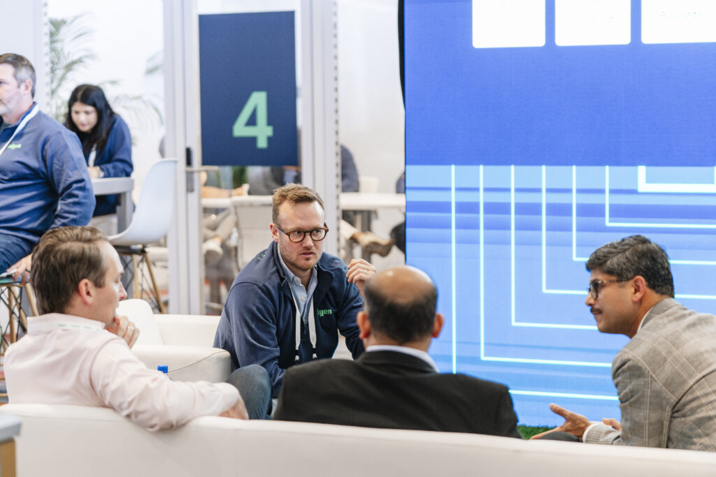 team member in conversation with attendees in a private lounge seating area during a trade show networking session.