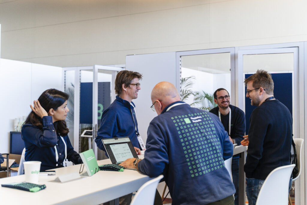 team at an expo booth interacting with event attendees around a high-top table with laptops and branded signage