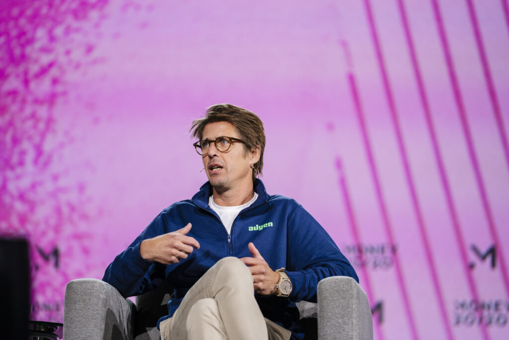Close-up of male panelist in branded attire speaking during a session at Money 20/20, with pink and black event graphics behind him.
