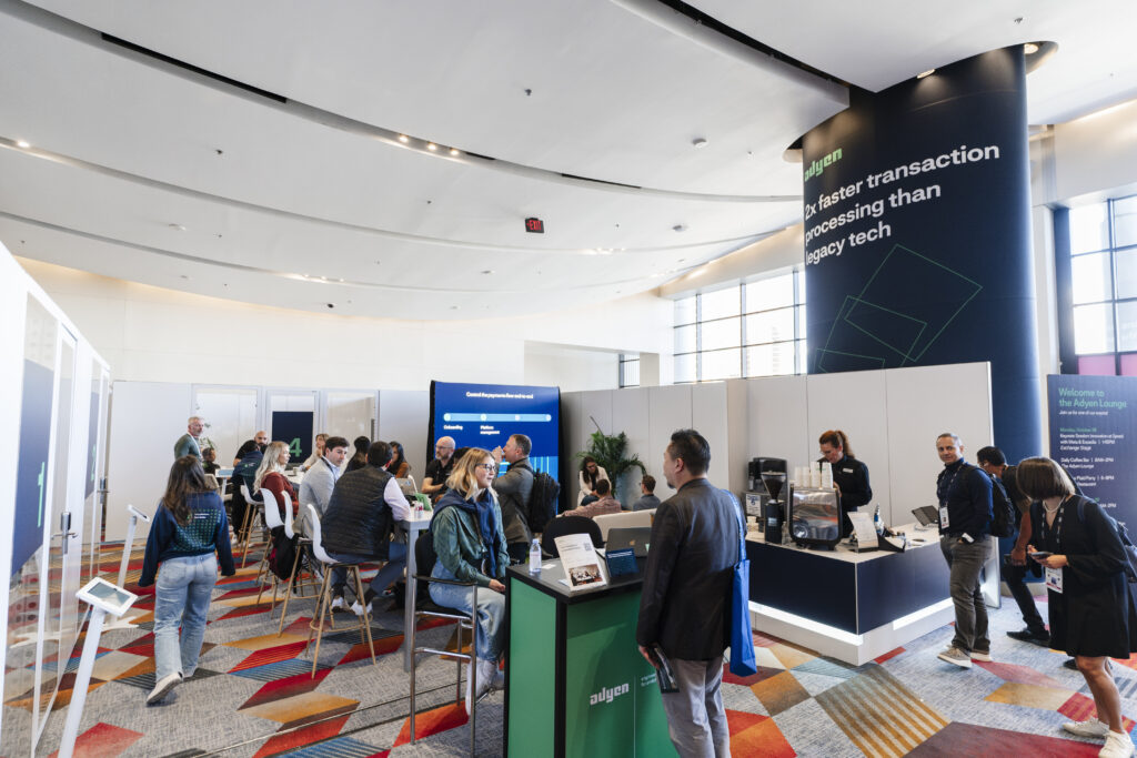Wide view of a packed lounge space at Money 20/20, filled with attendees networking at coffee bars and branded display stations.