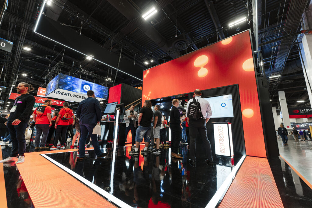 Modern CES-style exhibit booth with high-end AV technology and attendees engaging with booth representatives.