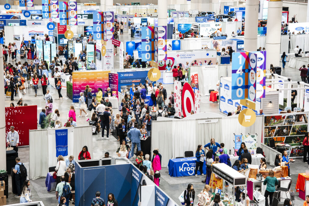 Crowded CES-style trade show floor with exhibitor booths, signage, and attendees walking through a busy convention hall.