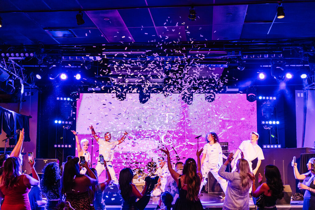 Performers entertaining guests on stage while attendees dance during an association reception at a conference.
