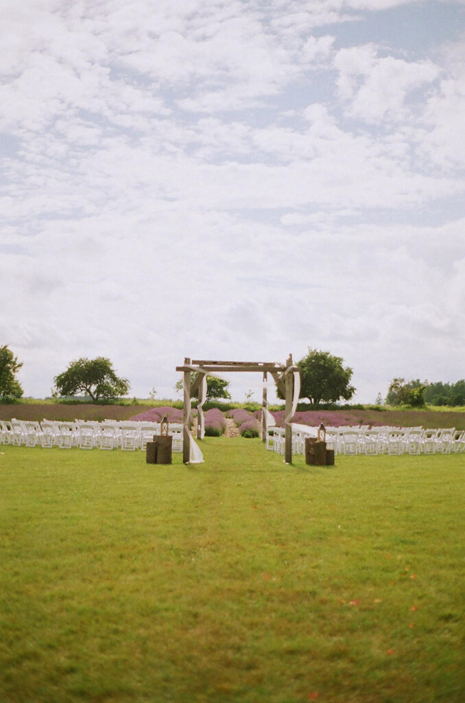 Outdoor summer wedding ceremony setup with rustic wooden arch and lavender fields in the background photographed on film by a traveling destination wedding photographer