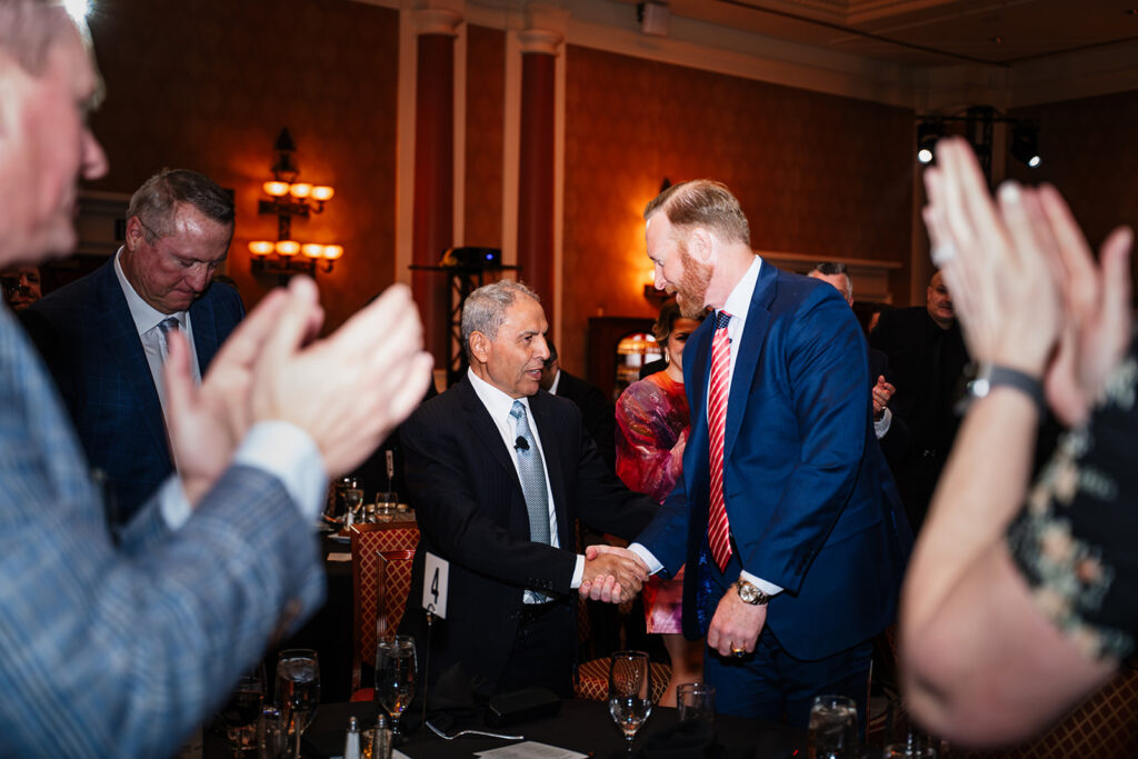 Association event photography captures a member receives recognition while peers applaud during a formal conference gathering, highlighting achievement and community.