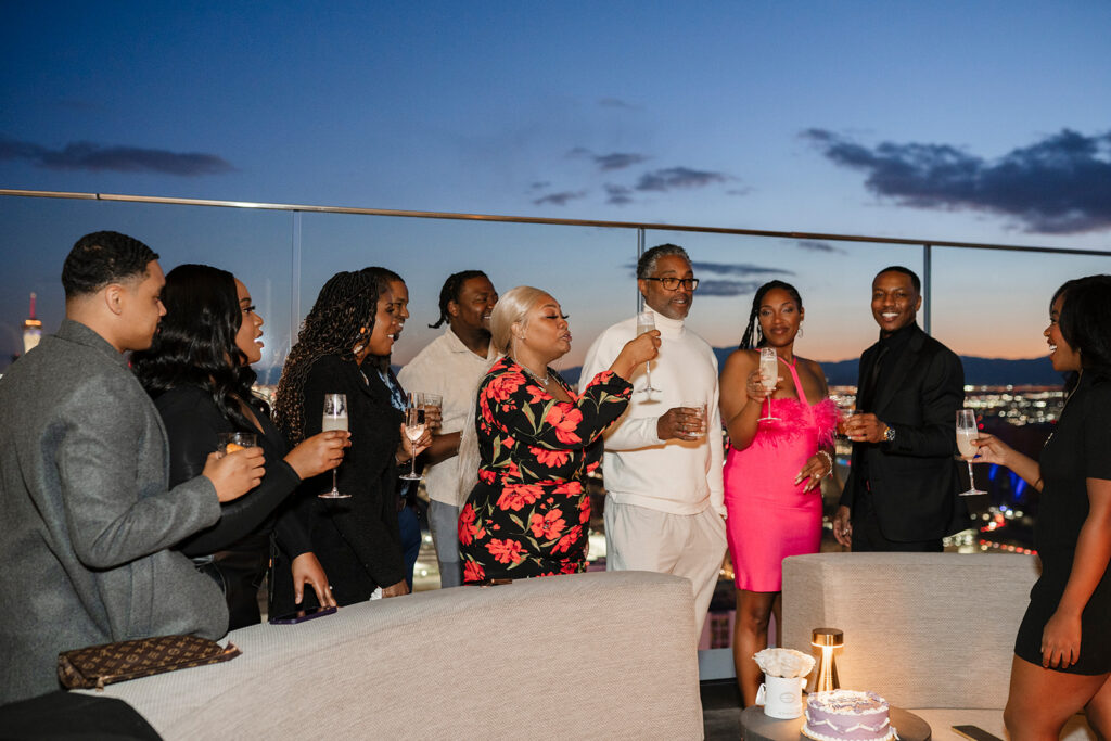 Wedding welcome dinner on a Las Vegas rooftop with guests toasting at sunset, capturing the extended celebration and guest-centered experience often included in a traditional wedding weekend.