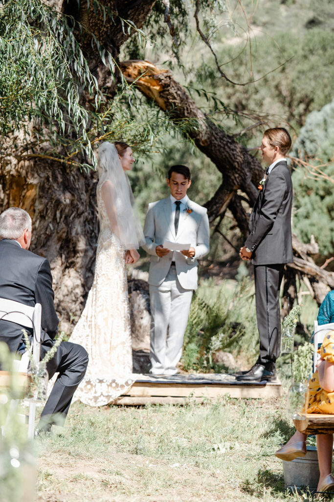 Bride and groom share an intimate moment under a large willow tree during golden hour portraits at a rustic outdoor destination wedding photographed by a destination Las Vegas wedding photographer