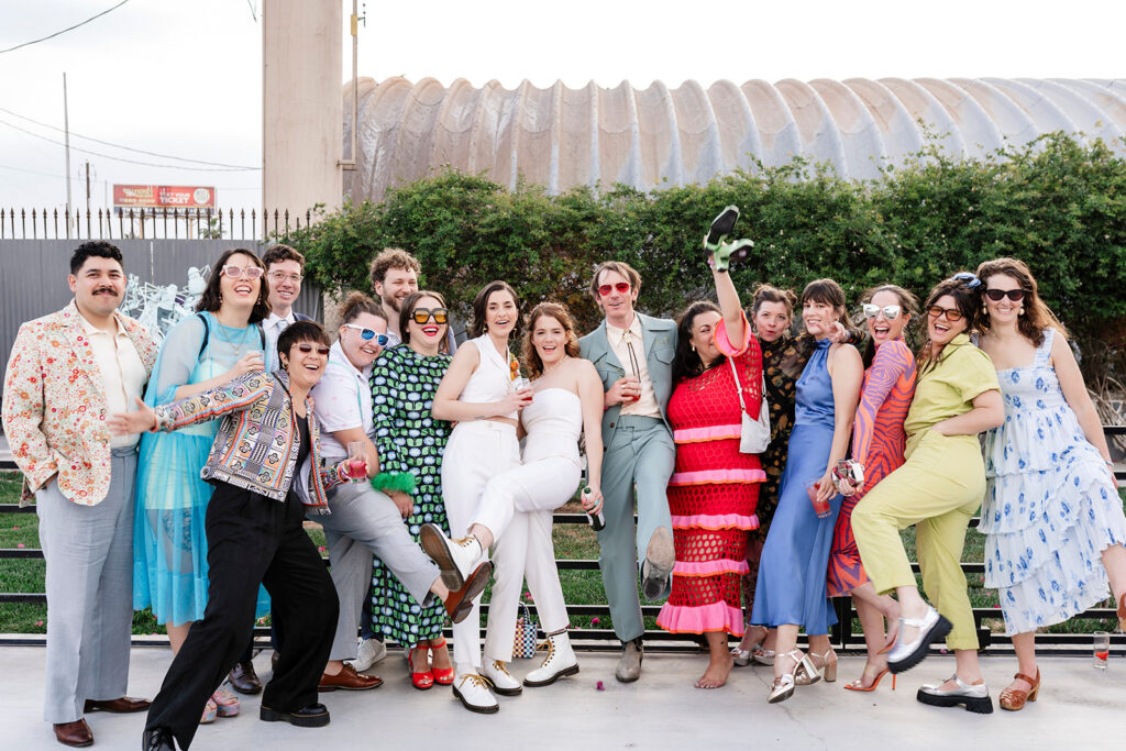 Brides laughing with a large group of friends and wedding guests during a high energy outdoor cocktail hour captured by True Colors Team large scale wedding photographers