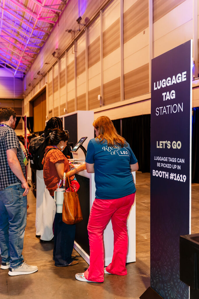 Conference attendees interact with a luggage tag station activation on the trade show floor in Las Vegas, highlighting experiential marketing and sponsor engagement at a corporate event.