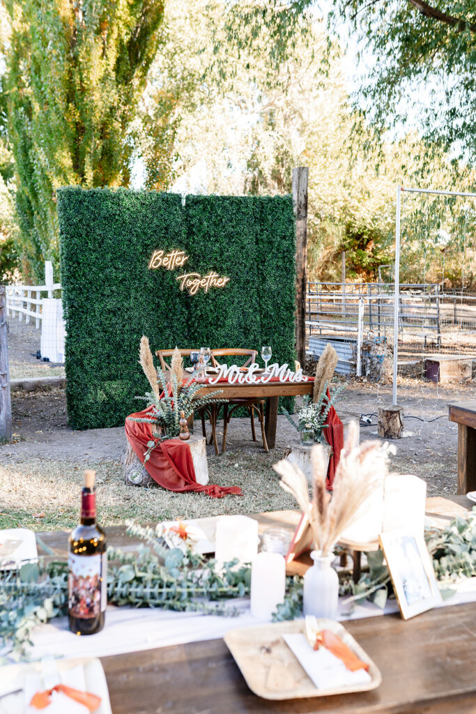 Outdoor wedding reception setup featuring a styled sweetheart table with floral accents and a decorative backdrop, illustrating the curated design elements often included in traditional weddings.