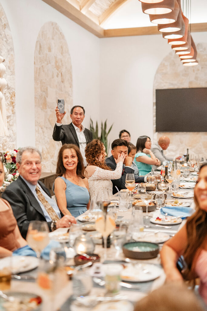 Couple sharing a candid moment at a small Las Vegas intimate wedding reception dinner surrounded by close family and guests at a long dining table.