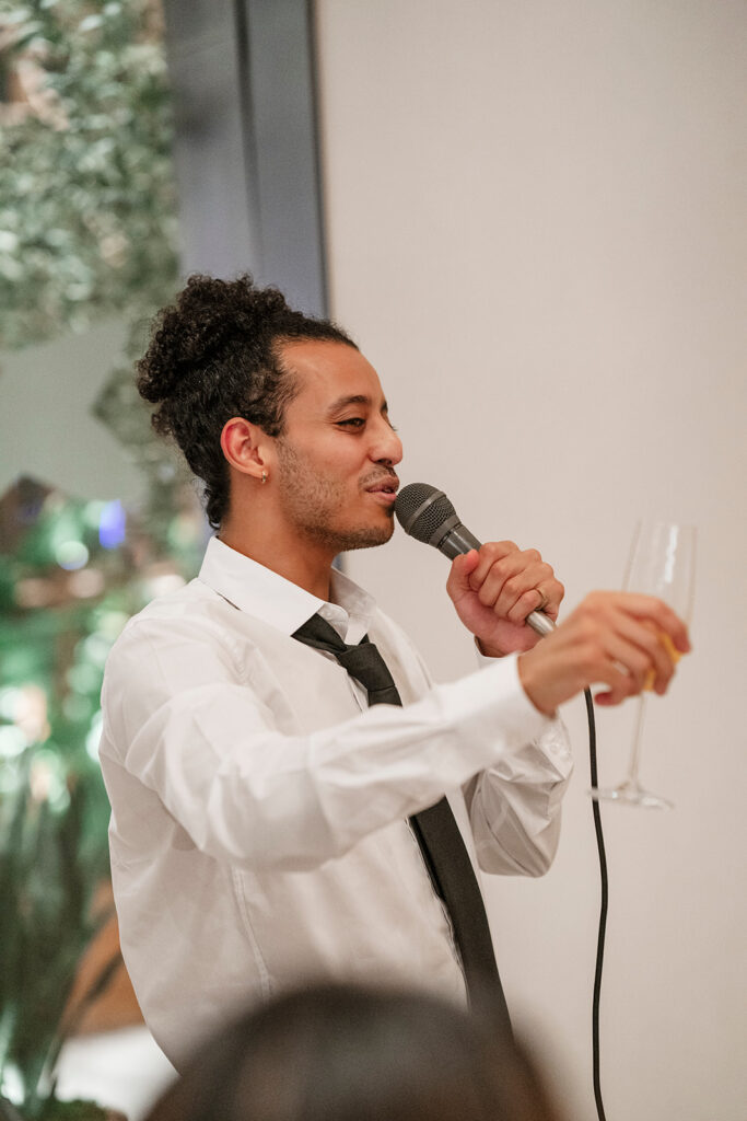Best man giving a heartfelt toast during an intimate Las Vegas wedding reception, holding a champagne flute in a modern indoor venue.