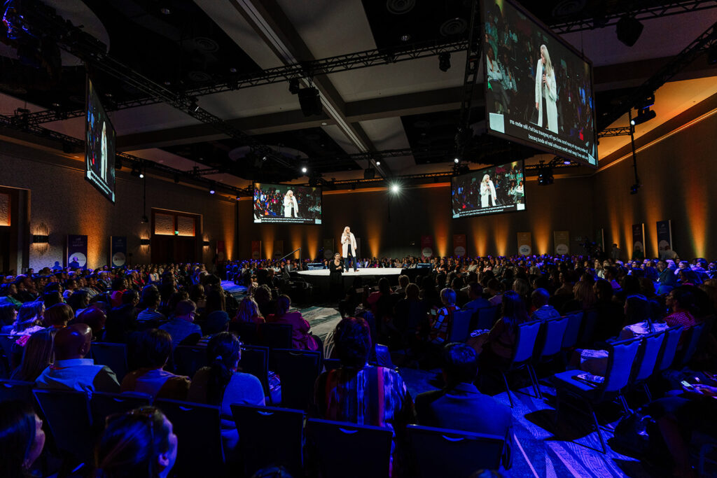 Photo of large general session with attendees listening and keynote speaker. 