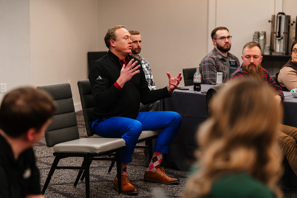 Association event photography captures member speaking during a small-group discussion session, illustrating collaborative dialogue and shared learning at a professional meeting.