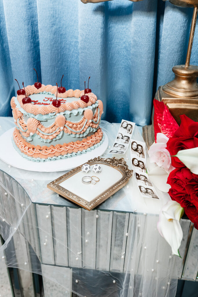 Styled wedding detail featuring a vintage-inspired heart cake, wedding rings, and photo booth strip, illustrating the curated design elements often included in a traditional wedding reception.
