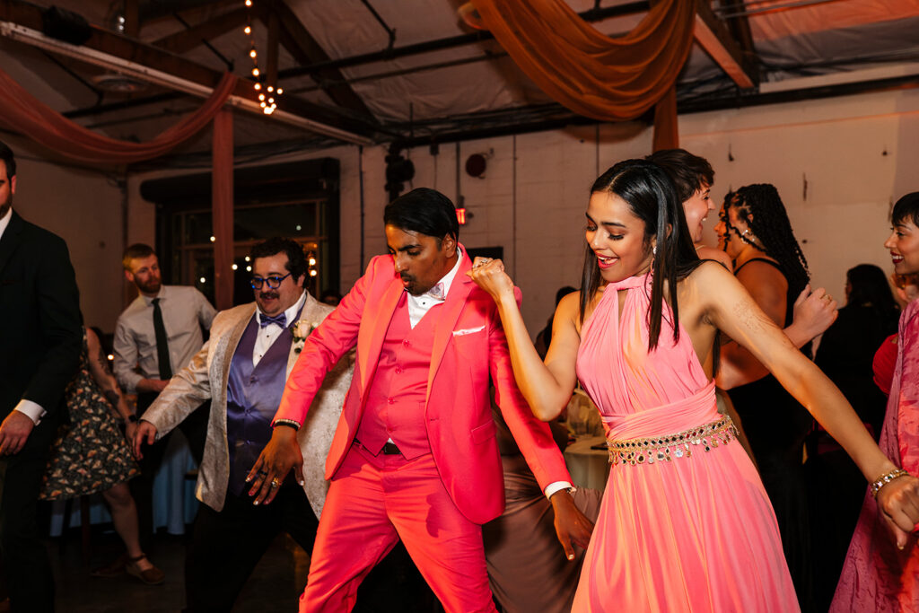 Wedding guests in bold colorful outfits dancing together on a packed dance floor at a large scale wedding reception photographed by True Colors Team