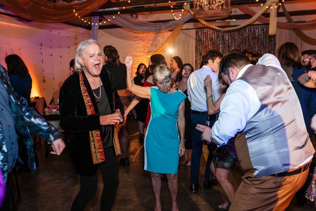 Multi generational wedding guests including older family members dancing and celebrating on a full dance floor at a large scale wedding reception photographed by True Colors Team