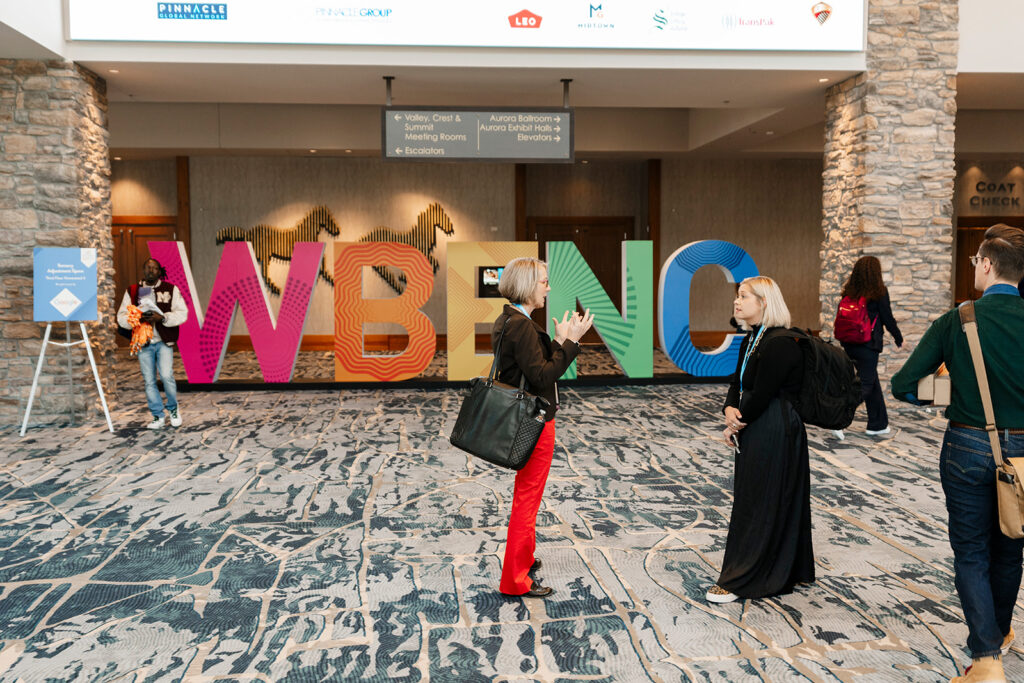 Attendees interact in a candid photo in front of event signage.