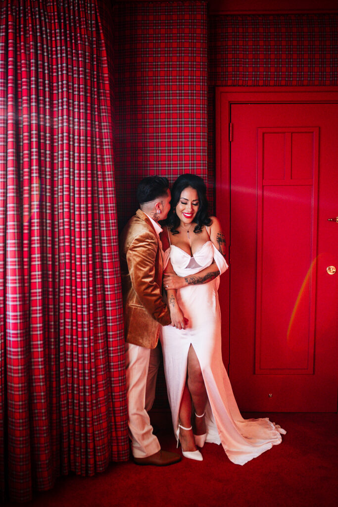 Brides sharing a romantic moment beside a red door inside a private Westgate suite during their Las Vegas elopement.