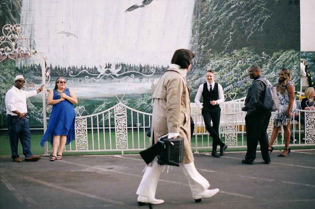 Film photo of Elvis impersonator walking past guests with groom smiling in the background at the Little White Chapel in Las Vegas.