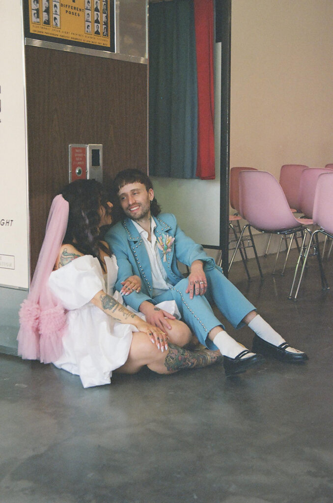 Elopement photographer documenting candid moment between newlywed couple in retro Las Vegas chapel, bride and groom sitting together laughing in intimate post-ceremony portrait.