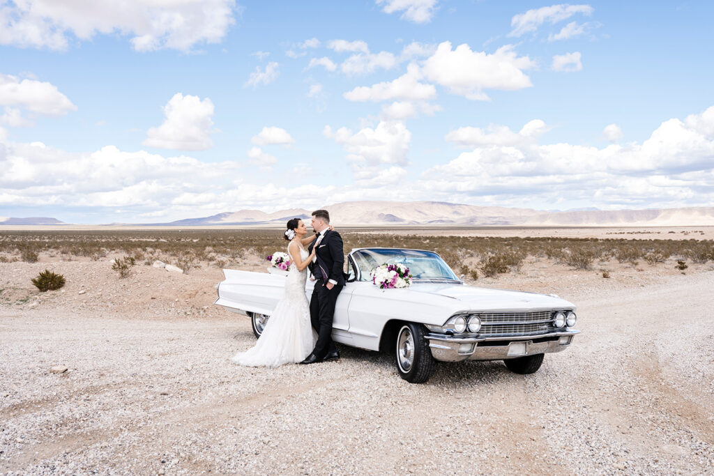 Elopement photographer photographing bride and groom leaning against classic Cadillac on a Las Vegas desert dry lake bed.