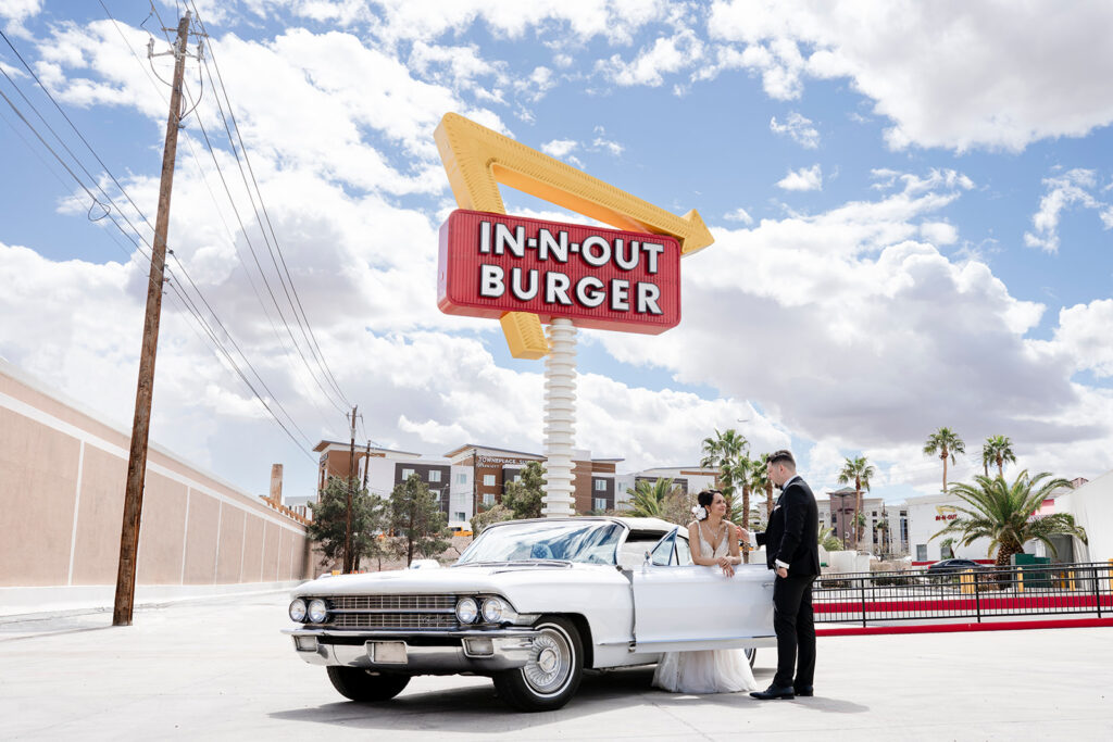 Elopement photographer capturing bride and groom with vintage white Cadillac beneath iconic In-N-Out Burger sign in Las Vegas.